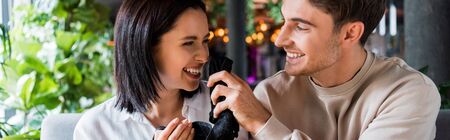 panoramic shot of happy man holding black napkin near smiling woman