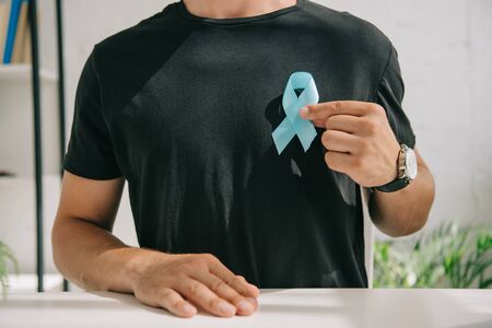 partial view of man in black t-shirt holding blue awareness ribbonの写真素材