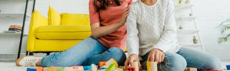 panoramic shot of babysitter and kid near toy blocks in living roomの写真素材