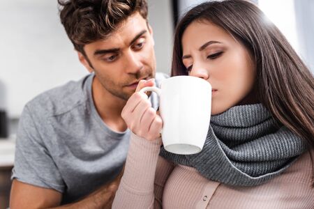 attractive and sick woman drinking tea and man looking at herの写真素材