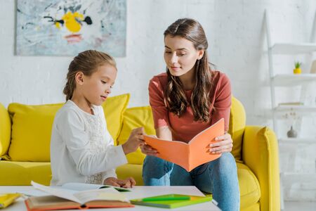 selective focus of attractive babysitter holding notebook near cute kid studying at home