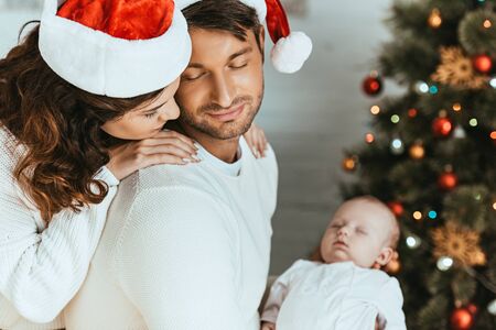 happy woman looking at sleeping baby over shoulder of husbandの写真素材
