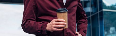 panoramic shot of man in coat holding paper cup while standing with hand in pocketの写真素材
