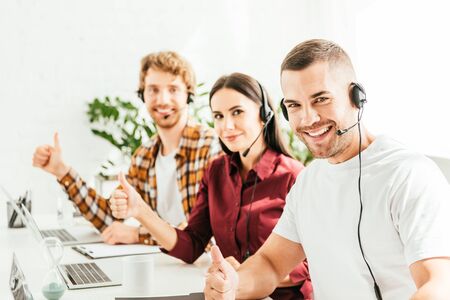 selective focus of happy broker showing thumb up near coworkers in officeの写真素材