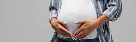 partial view of pregnant woman touching tummy isolated on greyの写真素材