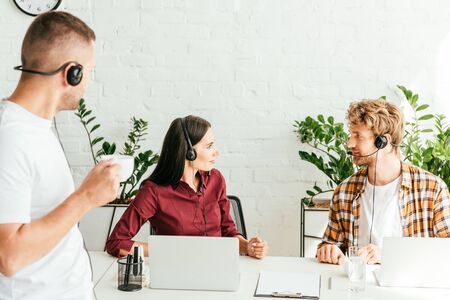 selective focus of brokers looking at each other near coworker with cupの写真素材