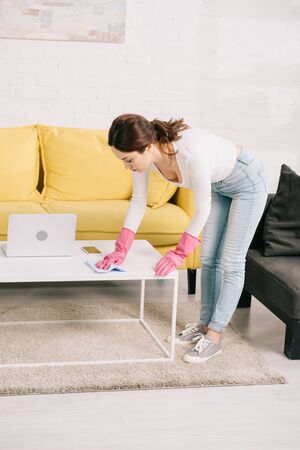 young housewife in denim jeans wiping table with rag near laptopの写真素材