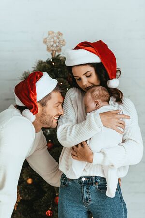 attractive woman in santa hat holding adorable baby near happy husbandの写真素材