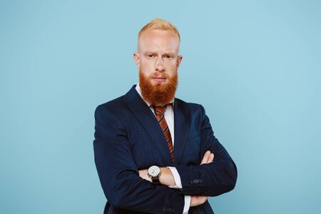 confident bearded businessman in suit with crossed arms, isolated on blueの写真素材