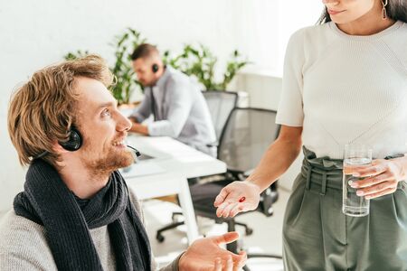 cropped view of broker giving pill to sick coworker in officeの写真素材