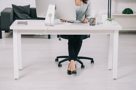 patial view of secretary in high heeled shoes sitting at workplace in office chairの写真素材