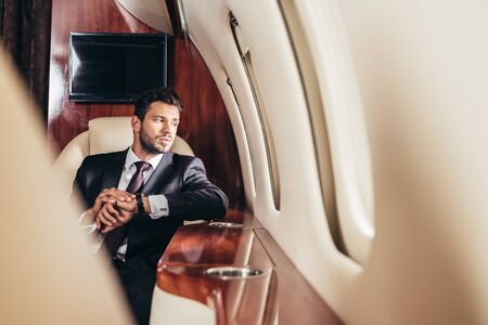 selective focus of handsome businessman in suit looking through window in private plane