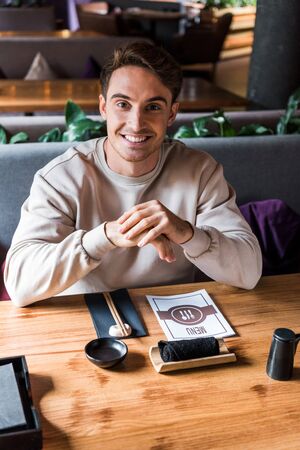 happy man sitting in sushi bar near table with menu
