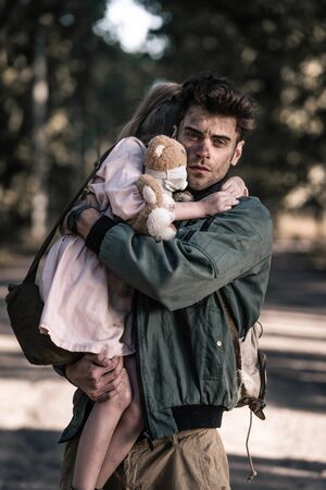 handsome and dirty man holding in arms child in chernobyl, post apocalyptic concept