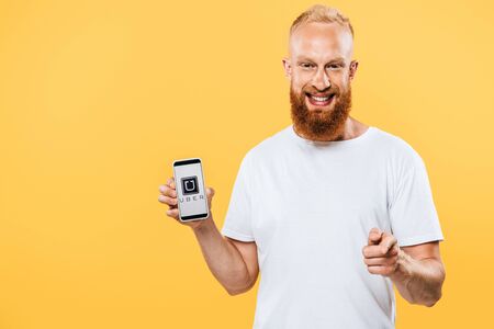 KYIV, UKRAINE - AUGUST 27, 2019: smiling bearded man presenting smartphone with uber app and...