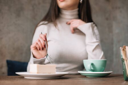 cropped view of woman eating cheesecake and drinking coffee in cafe