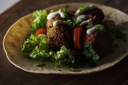 close up view of falafel with sauce on pita with vegetables in darkness