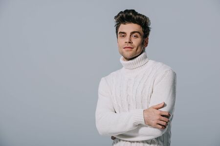 handsome stylish man posing in knitted sweater with crossed arms, isolated on greyの写真素材