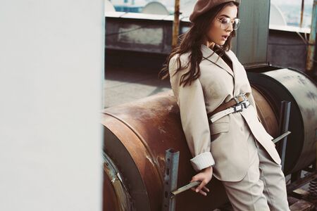 fashionable elegant model posing in beige suit and beret on roofの写真素材