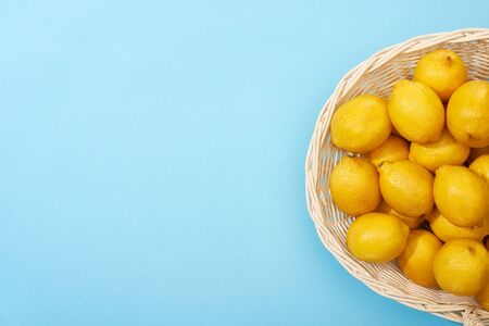 top view of ripe yellow lemons in wicker basket on blue background with copy spaceの写真素材