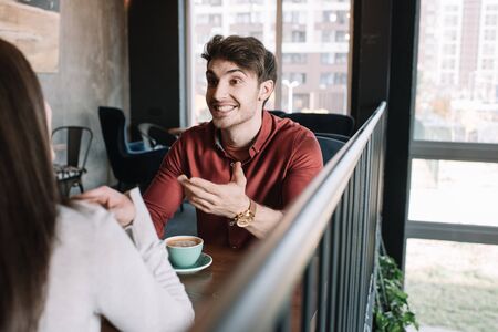 cheerful man talking to girl while drinking coffee on balcony in coffee shopの写真素材