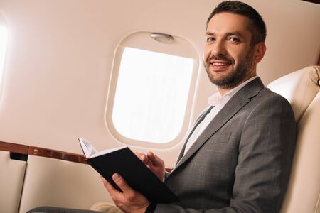 cheerful businessman holding notebook in private jet