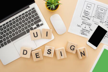 top view of gadgets near wooden blocks with ui design lettering, website design template and green plant on beige backgroundの写真素材