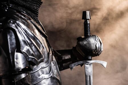 cropped view of knight in armor holding sword on black backgroundの写真素材