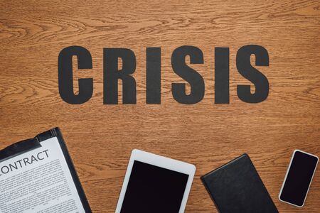 top view of word crisis near smartphone, digital tablet, notebook and clipboard with contract on wooden deskの写真素材