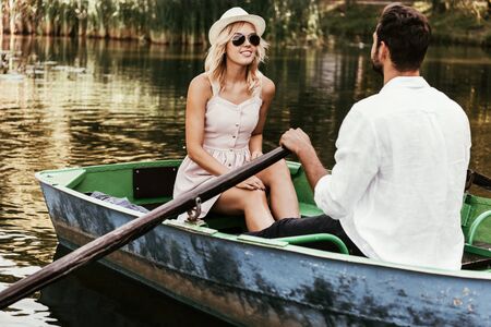 smiling girl in sundress and sunglasses looking at boating boyfriendの写真素材