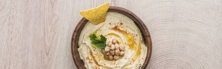 top view of delicious hummus with chickpeas and nacho in bowl on beige wooden table, panoramic shotの写真素材