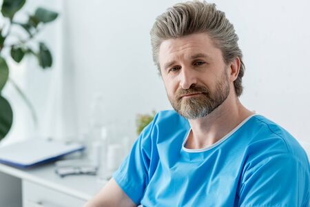 handsome patient in medical gown looking away in hospitalの写真素材
