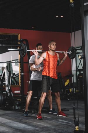 attentive trainer controlling african american sportsman lifting barbellの写真素材