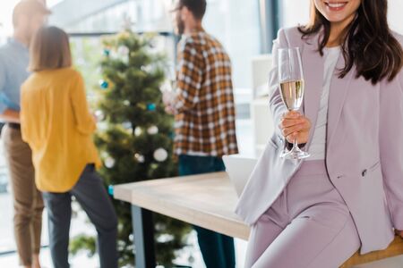 cropped view of businesswoman holding champagne glass near coworkers and christmas treeの写真素材