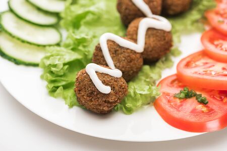 close up view of falafel with sauce on plate with sliced vegetables on white backgroundの写真素材
