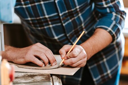 cropped view of carpenter drawing while holding pencil in workshopの写真素材