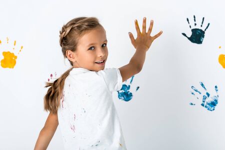 cheerful kid putting hand near hand prints on whiteの写真素材