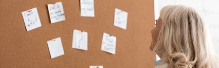 panoramic shot of senior woman with dyslexia looking at board with papersの写真素材