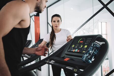 attentive trainer looking at sportsman running on treadmillの写真素材