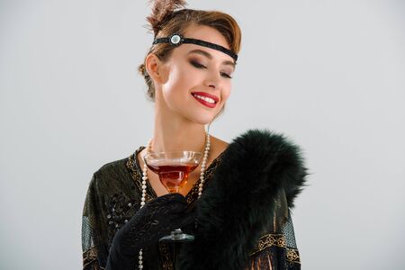 cheerful aristocratic woman holding glass with drink isolated on greyの写真素材