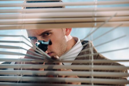 selective focus of dangerous gangster holding gun near window blindsの写真素材