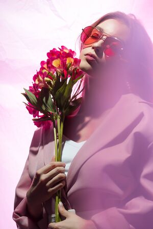 attractive woman in sunglasses holding flowers on whiteの写真素材