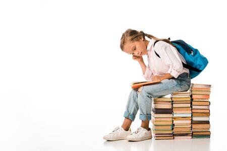 cute schoolkid sitting on books and reading on whiteの写真素材