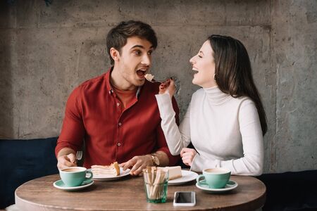 happy girlfriend feeding boyfriend with cheesecake in coffee shopの写真素材