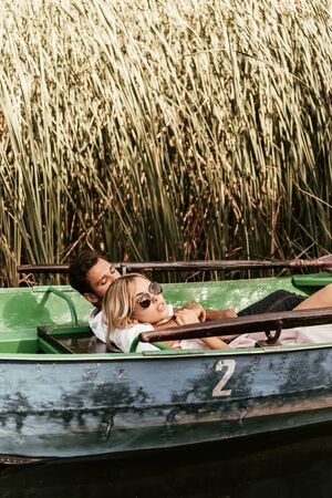 young couple relaxing in boat on river near thicket of sedgeの写真素材