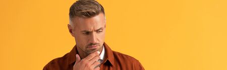 panoramic shot of handsome man touching face while thinking isolated on orange
