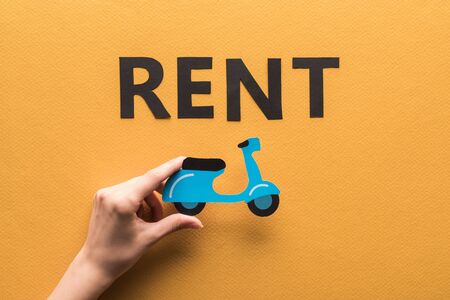 cropped view of woman holding paper cut scooter near rent lettering on orange backgroundの写真素材