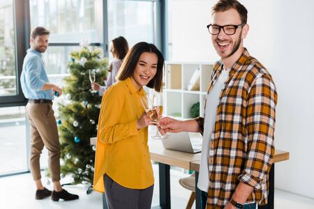 happy asian woman toasting champagne glasses with man near coworkers in officeの写真素材