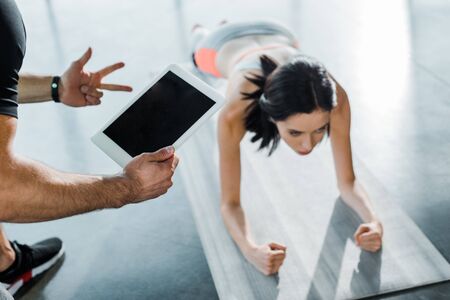 sportswoman doing plank and sportsman holding digital tablet in sports centerの写真素材