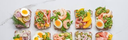 panoramic shot of fresh and delicious smorrebrod sandwiches on white marble surface